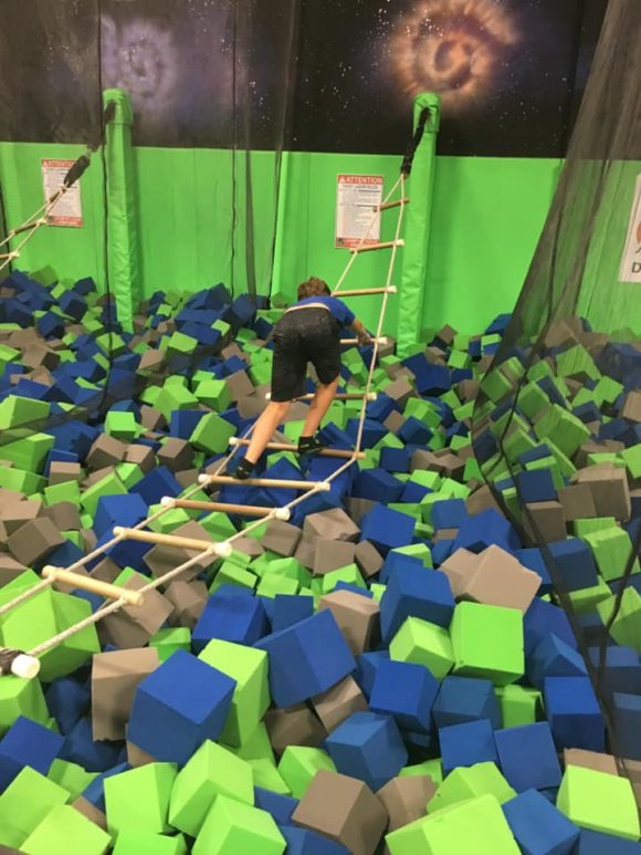 Nj trampoline park boy climbing rope ladder over foam square pit